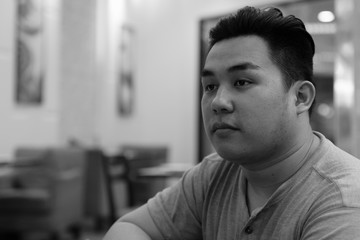 Face of young overweight Asian man thinking at the coffee shop