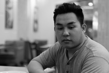 Stressed young overweight Asian man thinking at the coffee shop