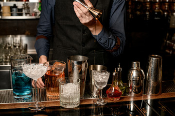Obraz na płótnie Canvas bartender carefully pours drink from jigger into shaker