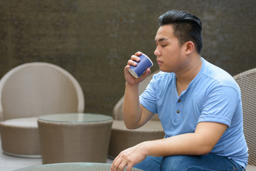 Young overweight Asian man drinking coffee at the coffee shop