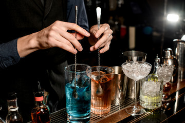 Close-up. Man bartender holds two spoons and mix cocktails with them