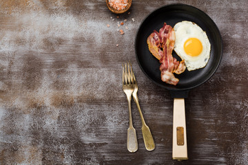 Traditional English breakfast with fried eggs and bacon in cast iron pan on dark concrete...