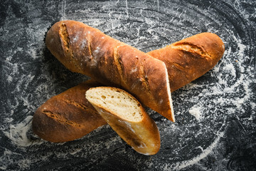 Traditional french baguette with flour on a dark background close-up.