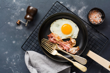 Traditional English breakfast with fried eggs and bacon in cast iron pan on dark concrete background. Top view.
