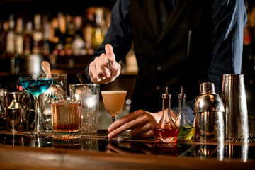 barman gently sprinkles on glass with sour cocktail.