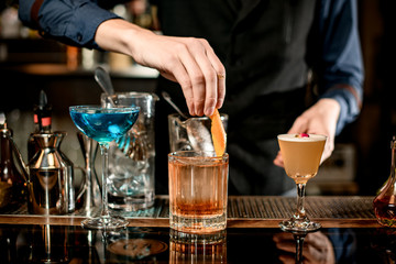 Barman's hand decorates cocktail glass with orange zest