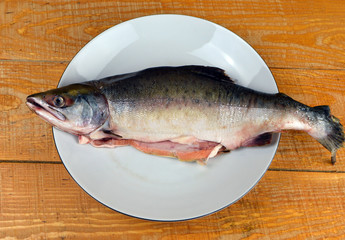 
gutted pink salmon lies in a plate on a wooden table