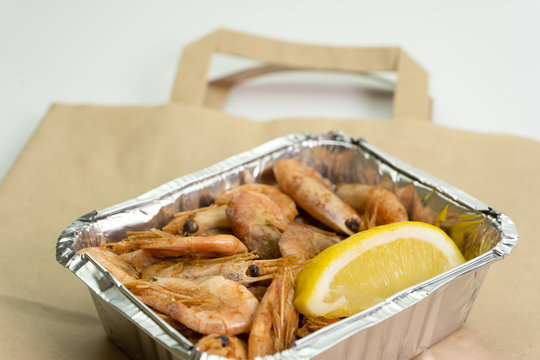 Close-up of shrimp in a foil box for delivery and a paper bag on a white background.