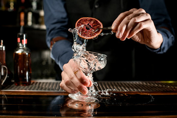 bartender holds beautiful transparent glass and decorate it with slice of citrus