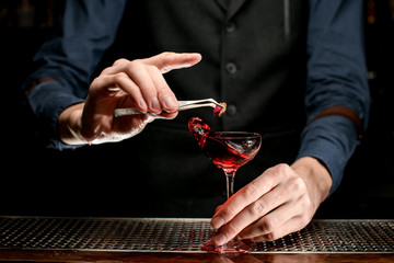 Male bartender decorates transparent glass with splash wine.
