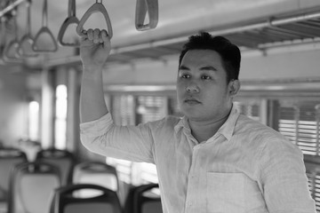 Young overweight Asian tourist man riding the train in black and white