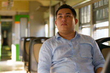 Young overweight Asian tourist man thinking inside the train