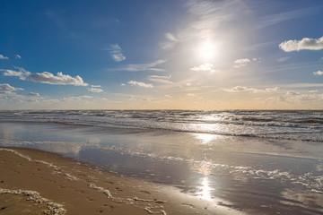 Die Sonne steht über dem Meer und wirft Reflektionen an den Strand
