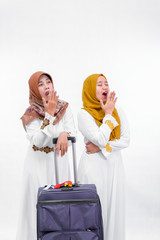 portrait of two muslim woman. mother and daughter or sister with suitcase smiling standing together waiting and look sleepy isolated over white background