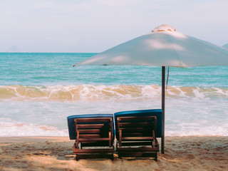 Chairs and umbrella on the beach near ocean. Winter vacation in hot places. Sunshine and moody sky