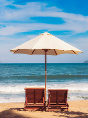 Chairs and umbrella on the beach near ocean. Winter vacation in hot places. Sunshine and moody sky