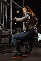 Obraz na płótnie Canvas low angle view of concentrated overweight girl doing arms extension exercise on fitness machine