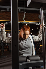 selective focus of overweight girl doing arms extension exercise on training machine