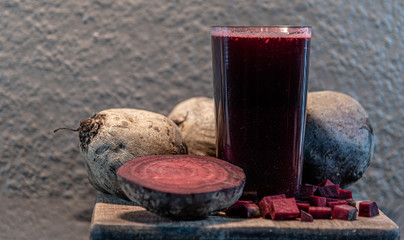 Glass with beet juice (Beta vulgaris) and tubers on wooden board