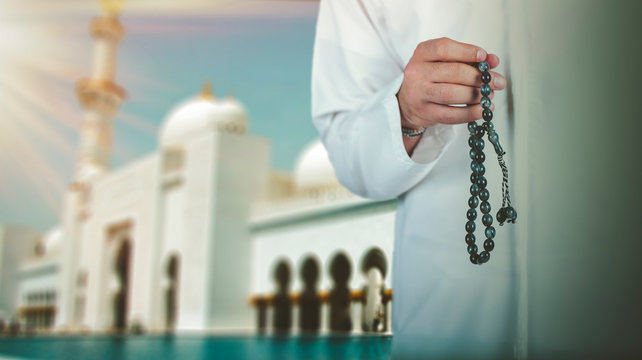 Arabic man hand holding a muslim rosary standing front a mosque. ramadan holy month, Ramadhan kareem concept.