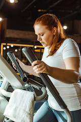 focused overweight girl training on step machine in gym