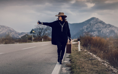 young woman on the empty roads with hat and suitcase