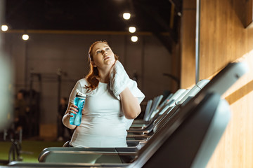 Fototapeta premium selective focus overweight girl wiping neck with towel while holding sports bottle