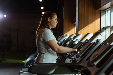 Fototapeta na wymiar side view of focused overweight girl training on treadmill in gym