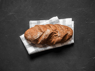 Loaf dark buckwheat bread on white textile napkin black table background. Fresh delicious homemade healthy bake. Bakery. Top view