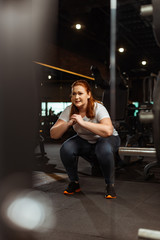 Obraz na płótnie Canvas selective focus of overweight girl squatting with clenched hands in gym