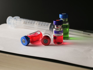 Coronavirus outbreak, Virus and recovery concept, a group of vaccine bottles with empty, red or green liquid and syringe placed on the white cover book
