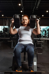 Fototapeta na wymiar focused overweight girl doing arms extension exercise on fitness machine