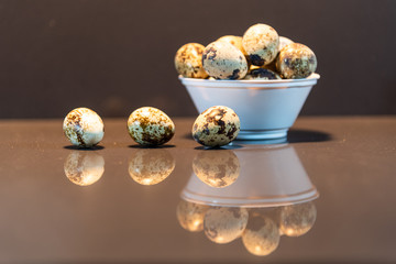 Quail eggs in a white pot scattered on a mirrored background