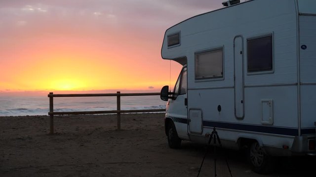 Camper vehicle camping on beach seashore at sunrise. Sea waves moving in slow motion. Spain, Costa Blanca, Alicante province