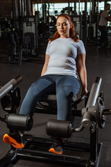 Obraz na płótnie Canvas focused overweight girl doing leg extension exercise on training machine