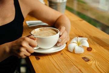 Beautiful woman hands with morning coffee mug in cafe with plumeria or frangipani flower.