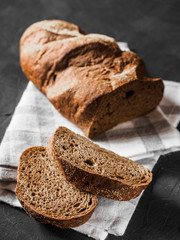 Loaf dark buckwheat bread on white textile napkin black table background. Fresh delicious homemade healthy bake. Bakery