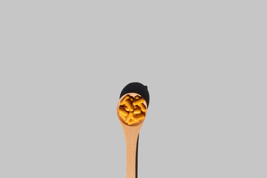 wooden spoon with turmeric curcumin capsules on grey background