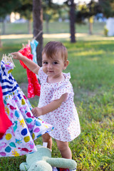vertical portrait of a cute baby girl in a summer dress against the background of summer nature and clothes that are dried in the air