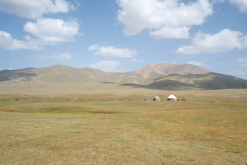 Fototapeta na wymiar Yurts on the empty plains with smooth hills of the Song Kul plateau in Kyrgyzstan during summer