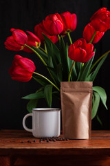 Fototapeta na wymiar White coffee cup with amazing blooming red tulips bouquet on black background. Dark moody low key minimalism style flowers and hot drink mug photo banner. Stylish greeting card copy space.Good morning
