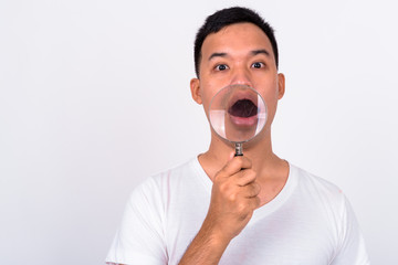 Face of young Asian man using magnifying glass