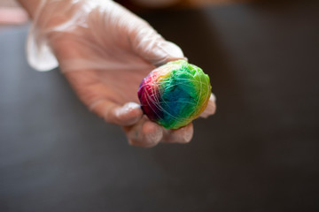 Colorful eggs for Easter in a woman's hand. Egg in multicolored paper rewound with white thread for...