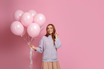 Smiling carefree girl posing with pastel pink air balloons isolated over pink background. Beautiful happy young woman on a birthday holiday. space for text