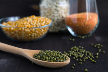 Healthy lifestyle. green mung beans with wooden spoon on a black background.  different kinds of groats: yellow corn, white beans and green mung in jars on a wooden table.