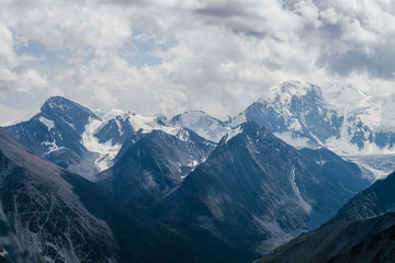 Awesome landscape with huge glacial mountains in bad cloudy weather. Low stormy clouds touch top of snowy mountain with glaciers. Storm is coming due to mountains. Gloomy overcast atmospheric scenery.
