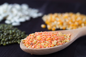close-up red lentils in wooden spoon on a black background. wooden spoon with lentils. different kinds of groats: yellow corn, white beans and green mung on a wooden table. Healthy lifestyle.