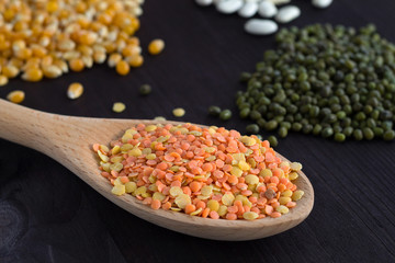 Fototapeta na wymiar close-up wooden spoon with lentils. different kinds of groats on a wooden table. Healthy lifestyle. red and yellow lentils, corn, white beans and mung on a black background.