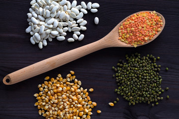red and yellow lentils, corn, white beans and green mung on a black background. wooden spoon with lentils. different kinds of groats on a wooden table. Healthy lifestyle. top view