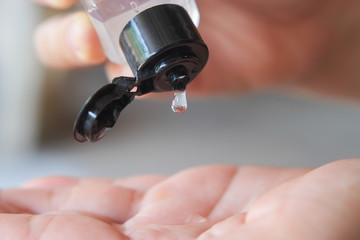 Alcohol gel from plastic bottle is dripping on their hands to clean and kill germs close-up.